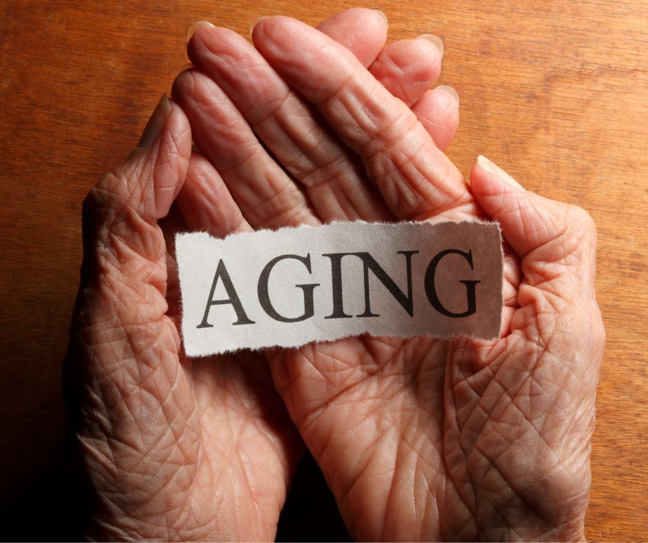Wrinkled hands holding a torn piece of paper with the word ‘Aging.